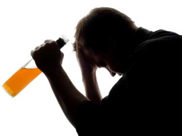 Silhouette of a man with head bowed and a bottle of alcohol